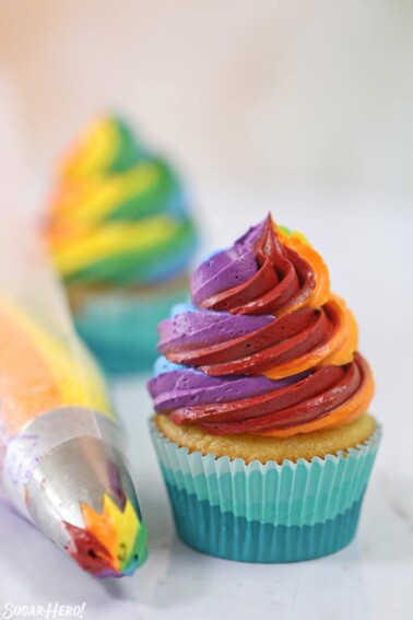 Cupcake with swirled rainbow frosting and a rainbow piping bag next to it
