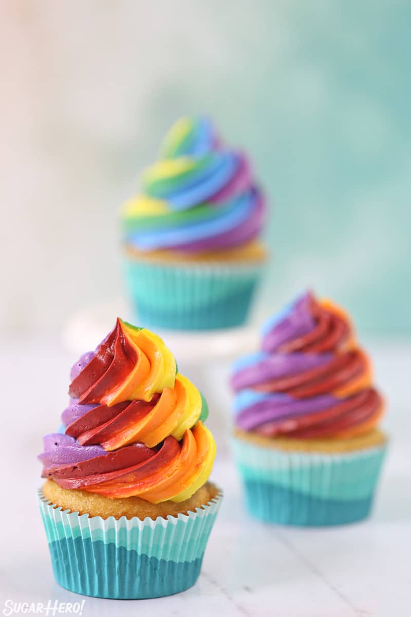 Three cupcakes with colorful rainbow icing swirls