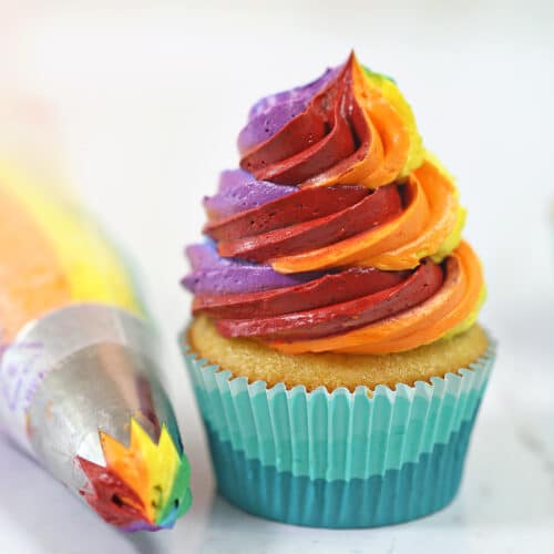Cupcake with colorful rainbow icing and a piping bag next to it