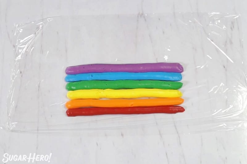 Six stripes of colorful rainbow frosting on plastic wrap