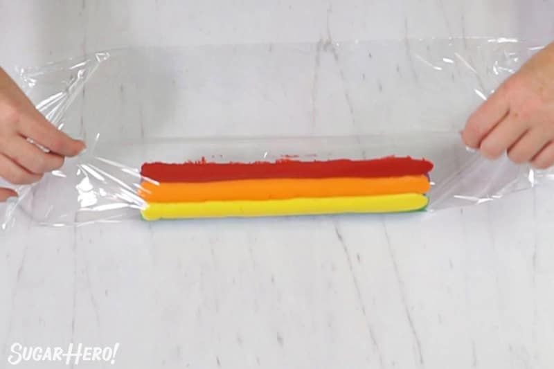 Rolling up rainbow frosting in plastic wrap