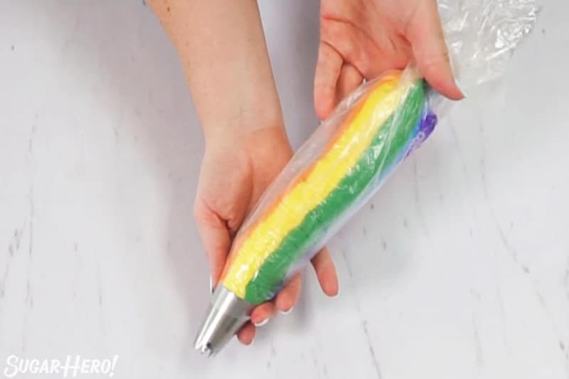 Hands holding piping bag with rainbow frosting inside