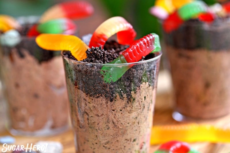 Close-up of cup of dirt pudding with Oreo crumbs and colorful gummy worms on top.