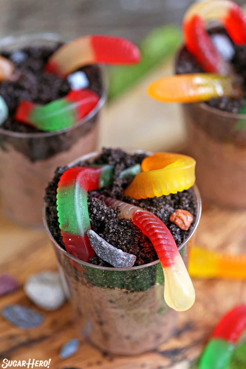 Overhead shot of 3 cups of dirt pudding, with Oreo crumbs and gummy worms on top.