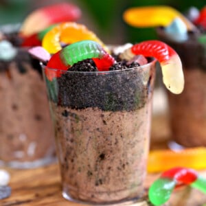 Three chocolate pudding cups with Oreo crumbs and gummy worms on top.