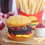 Close-up of Hamburger Cupcake on brown parchment with sugar cookie french fries in the background.