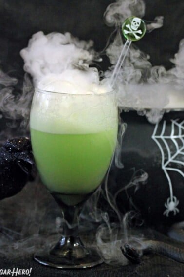 Goblet of green punch with smoke coming out the top and a black cauldron in the background