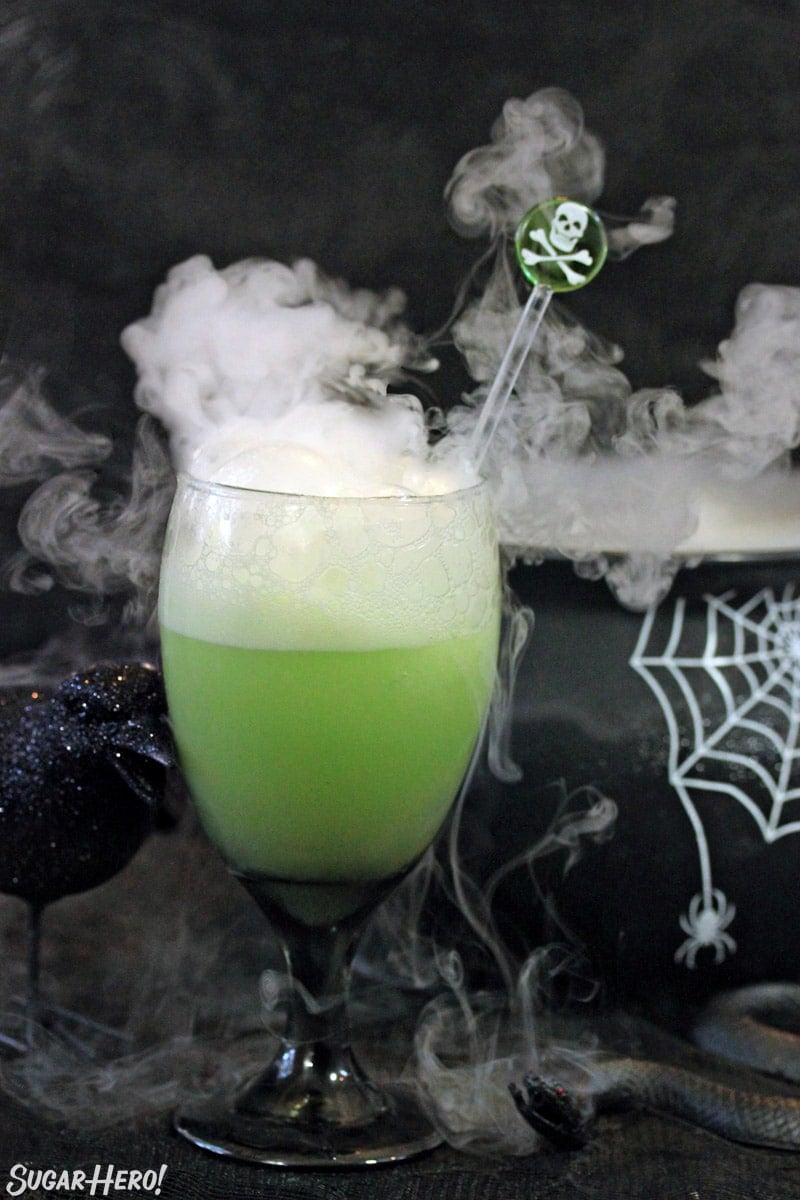 Goblet of green punch with smoke coming out the top and a black cauldron in the background