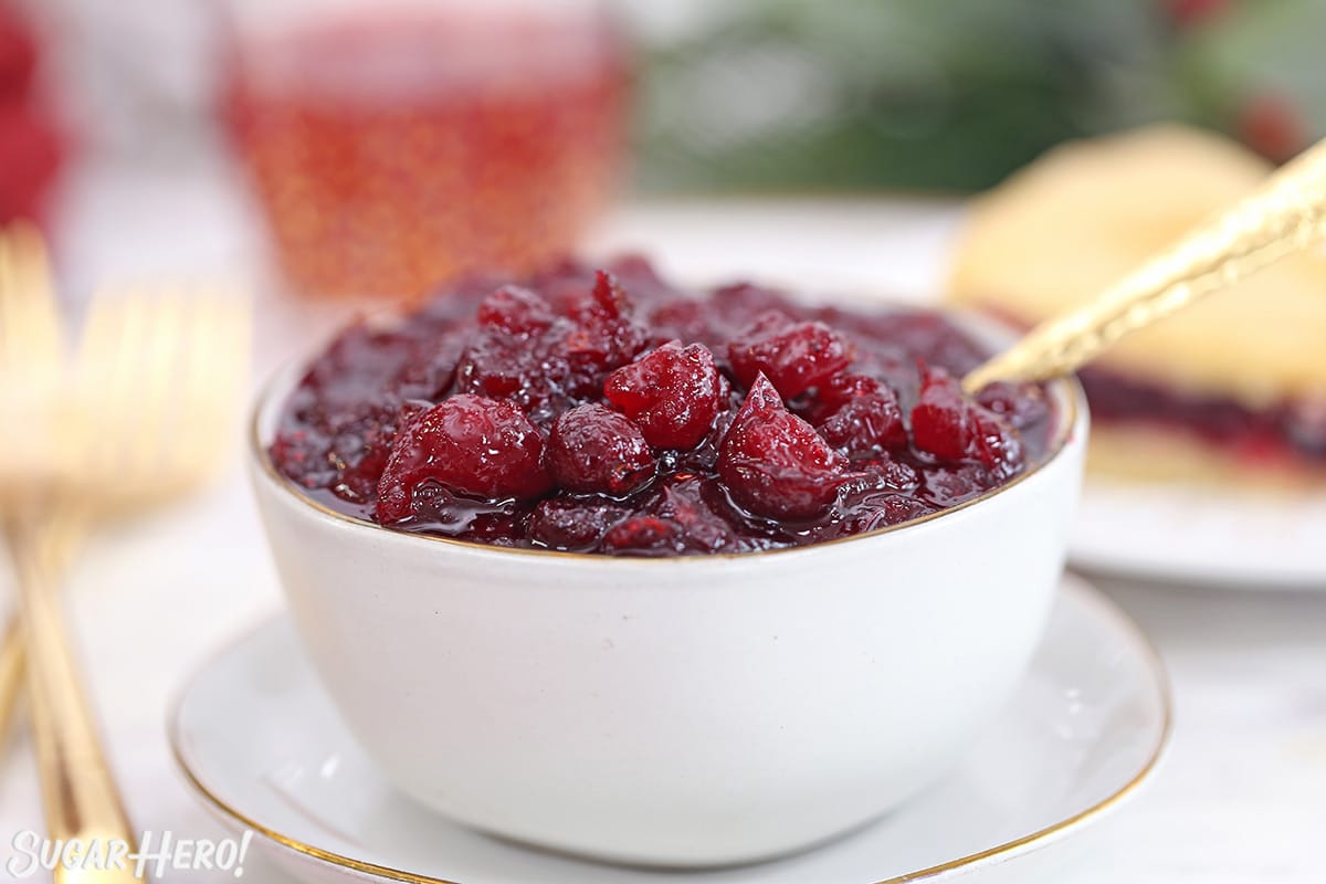 Homemade cranberry sauce in a white bowl with a gold spoon.