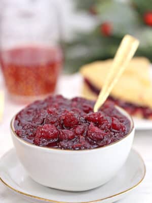 Homemade cranberry sauce in a white bowl with a gold spoon sticking out