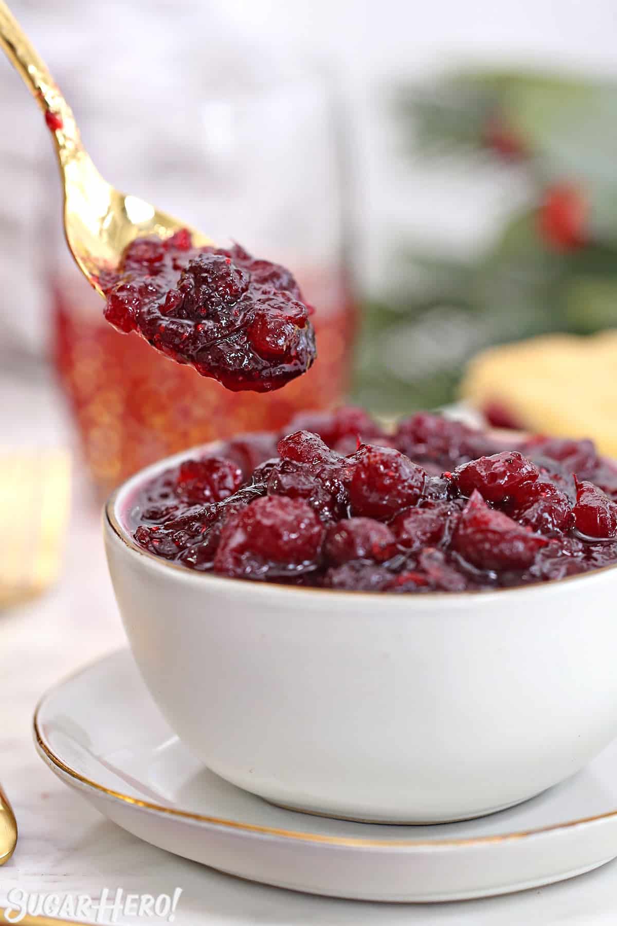 Fresh cranberry sauce in a white bowl with a gold spoon taking a scoop of sauce.