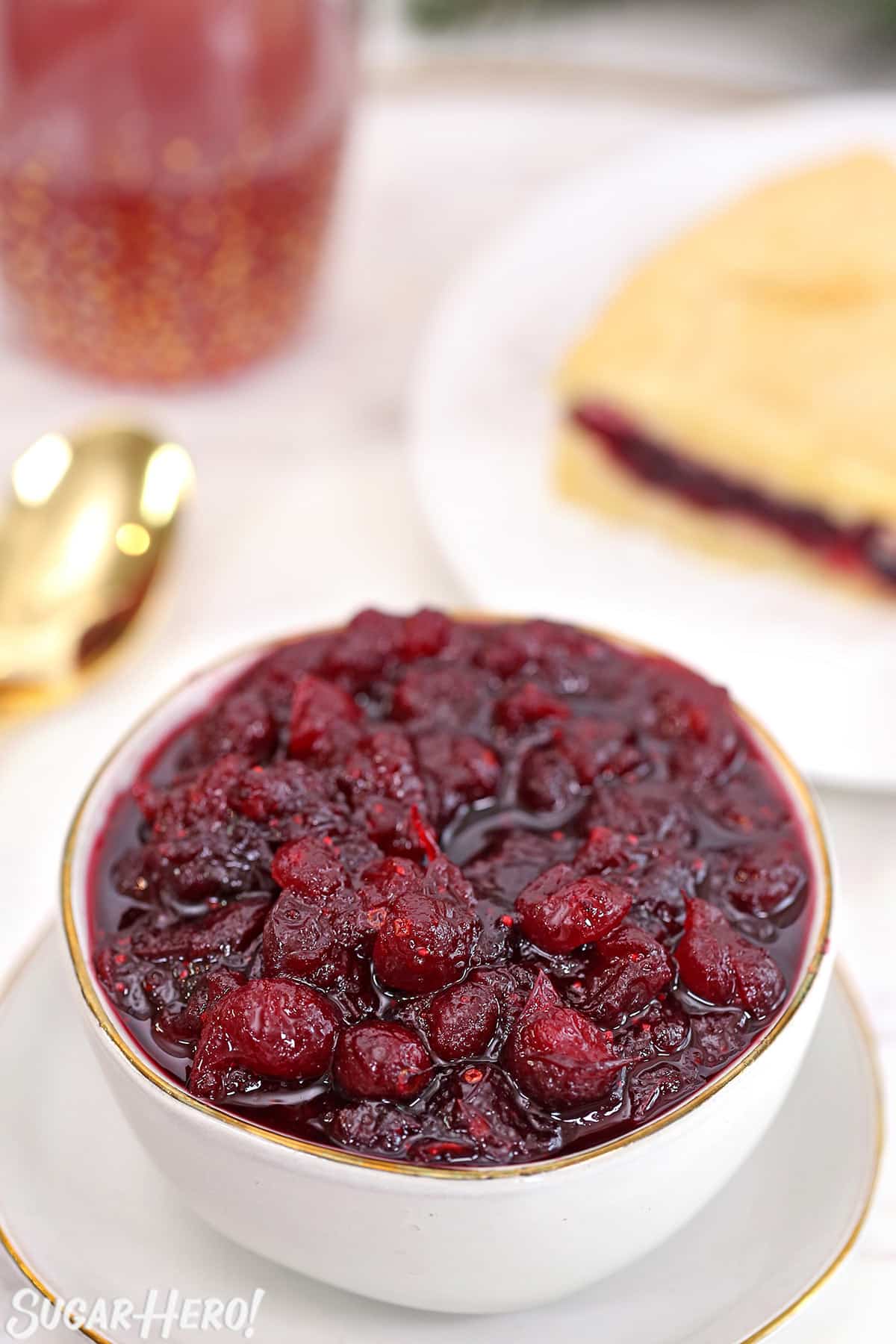 Overhead shot of homemade cranberry sauce in a small white bowl with cranberry cake in the background.