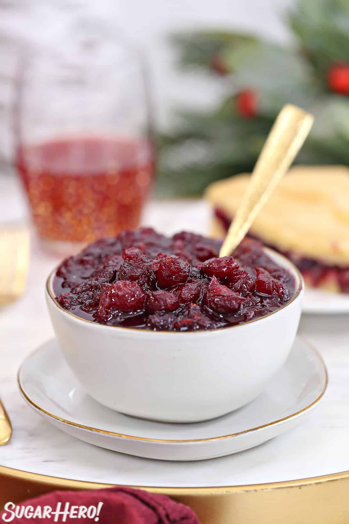 Homemade cranberry sauce in a white bowl with a piece of cranberry cake behind.