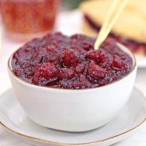 Homemade cranberry sauce in a white bowl with a gold spoon.