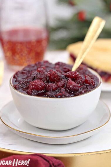 Homemade cranberry sauce in a white bowl with a piece of cranberry cake behind.