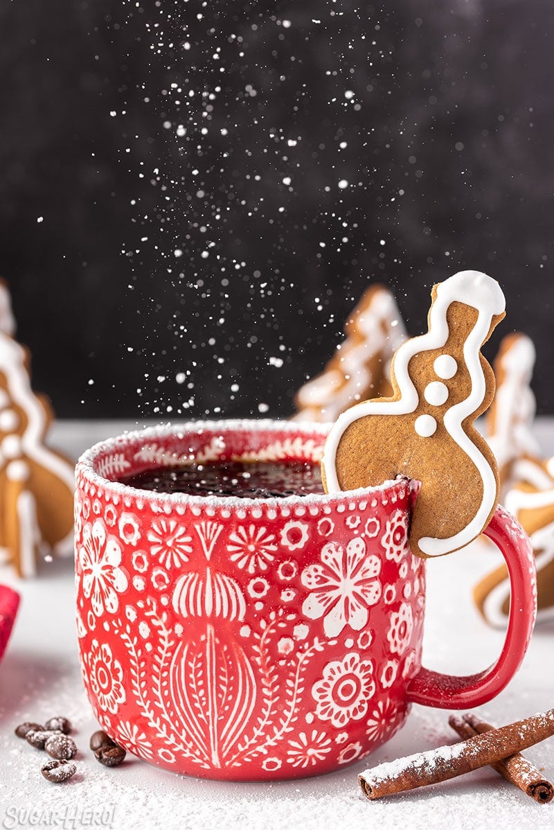 Snowman-shaped Gingerbread Cookie Mug Topper on a red mug with powdered sugar raining down