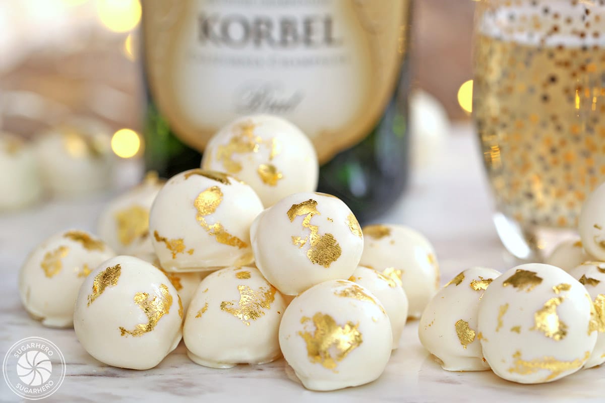 Champagne White Chocolate Truffles with gold leaf decorations, in front of a bottle of champagne