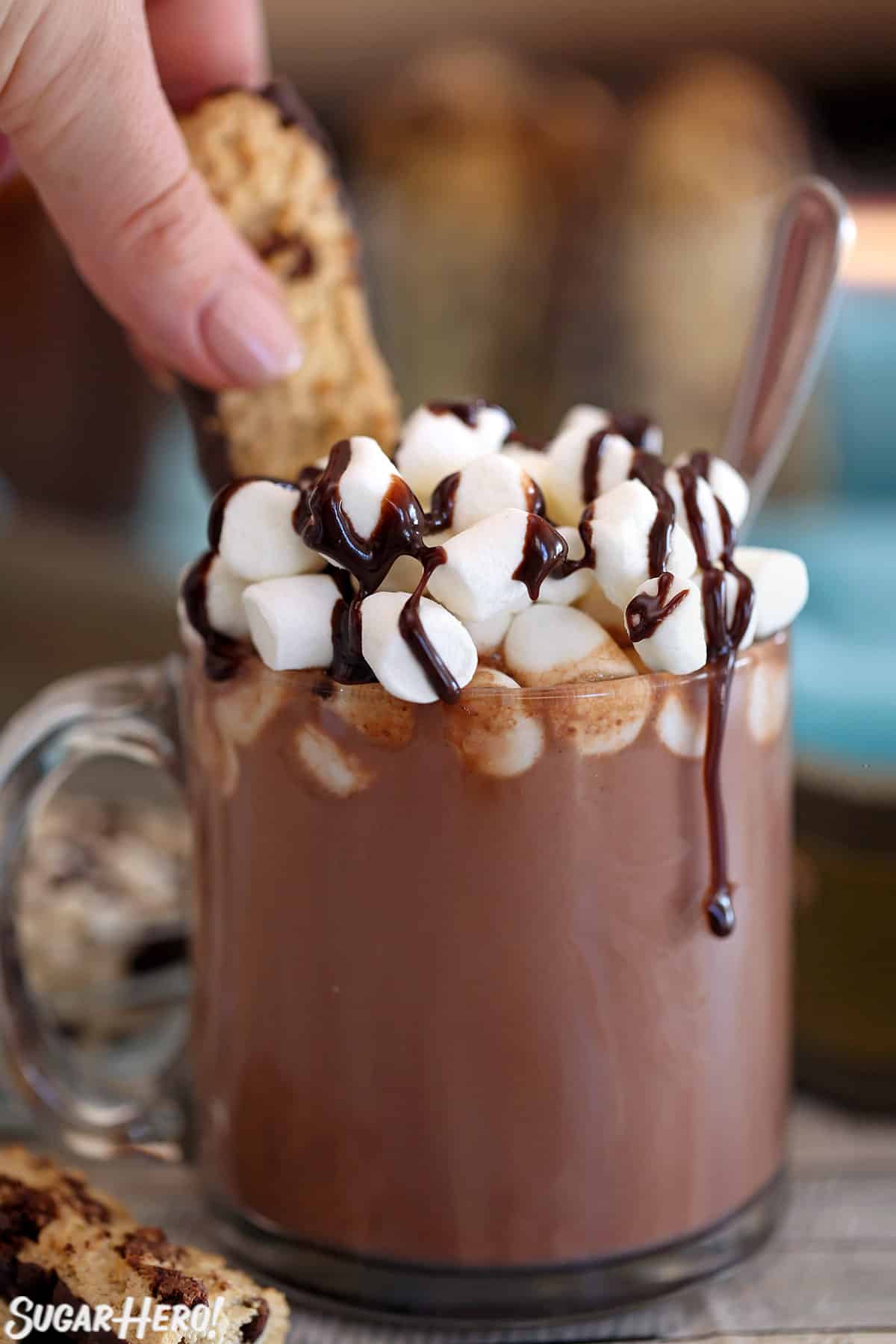 Hand dunking a cookie into Slow Cooker Hot Chocolate in a glass mug