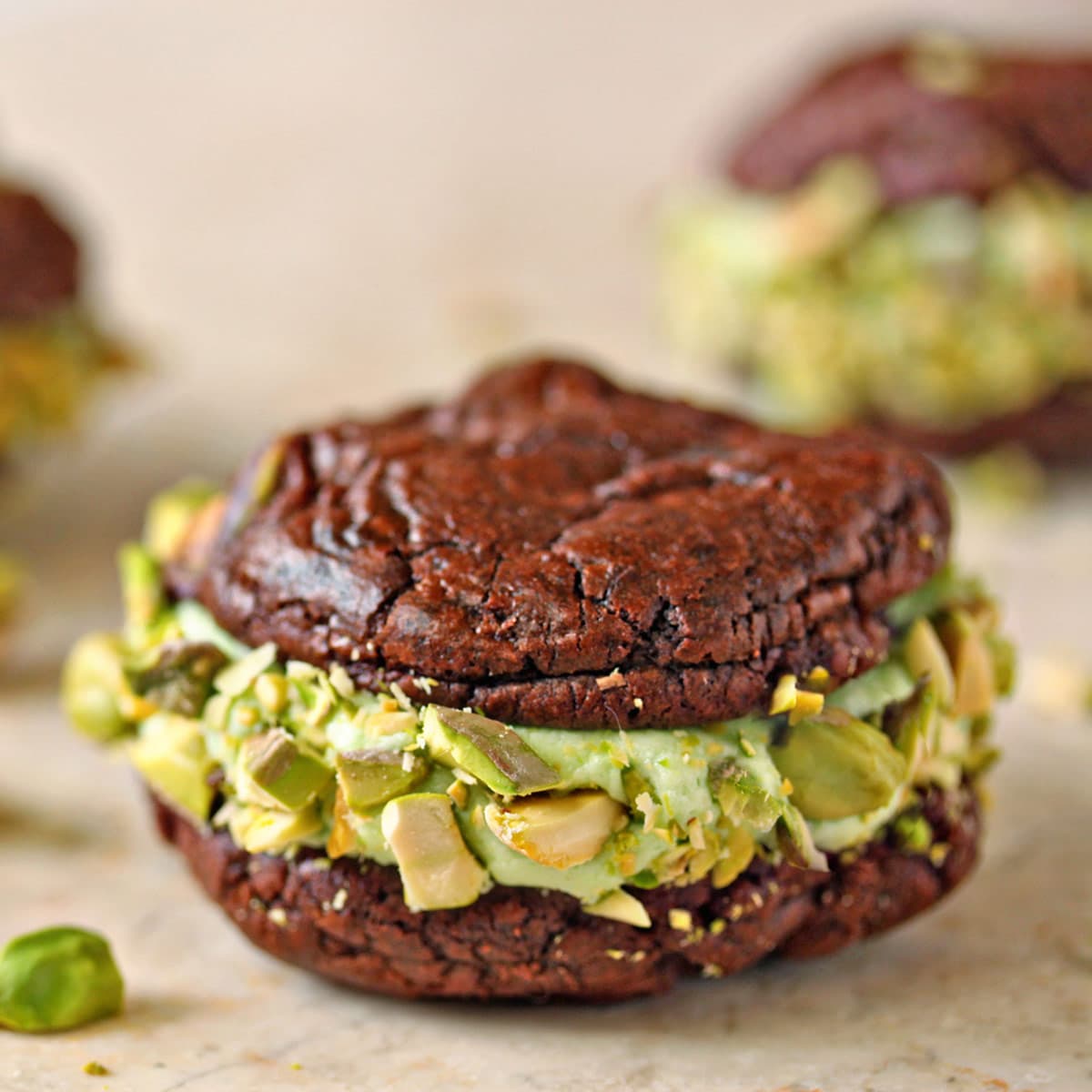 Chocolate Pistachio Sandwich Cookie on a marble board with pistachios scattered around
