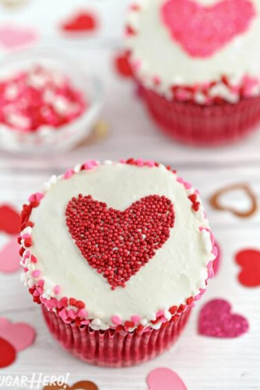 White cupcake with heart sprinkles around the edge and a heart-shaped sprinkle shape in the center