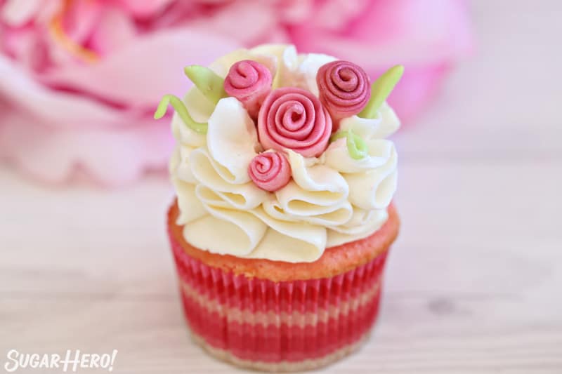 Close up of cupcake with white ruffled frosting and pink fondant flowers