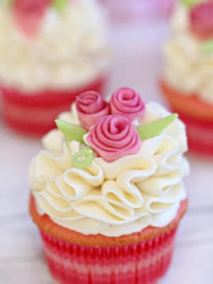 Pink cupcake with white ruffled frosting and pink fondant flowers.