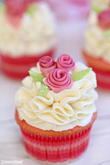 Pink cupcake with white ruffled frosting and pink fondant flowers.