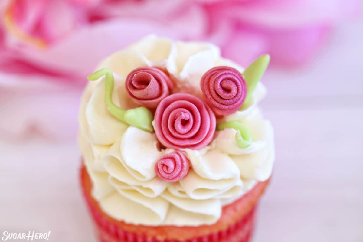 Close up of cupcake with white ruffled frosting and pink fondant flowers