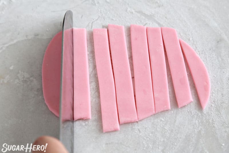 Knife slicing pink fondant into long narrow strips