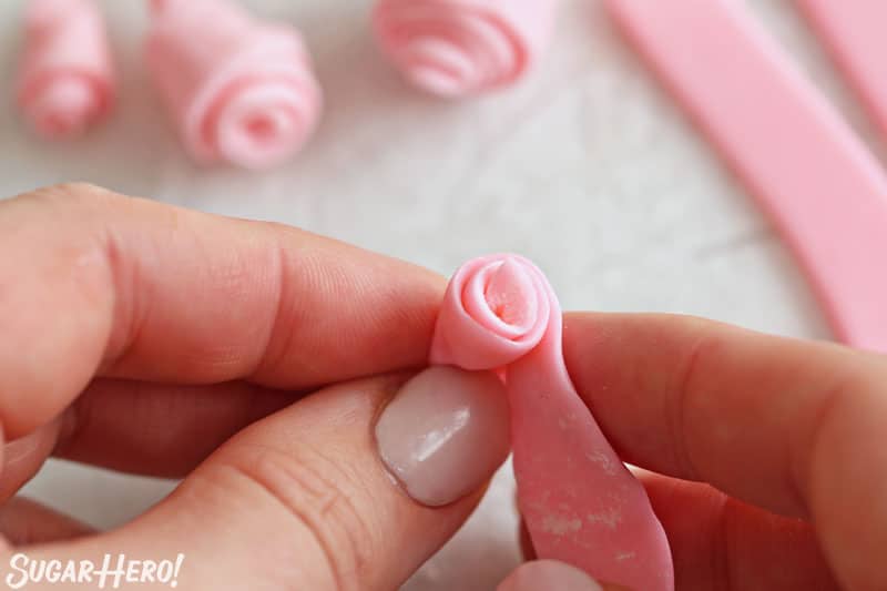 Hands rolling up a ribbon of pink fondant into a rose shape