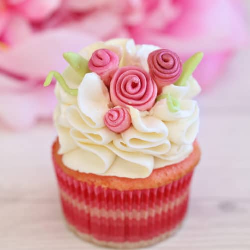 Close up of cupcake with white ruffled frosting and pink fondant flowers.