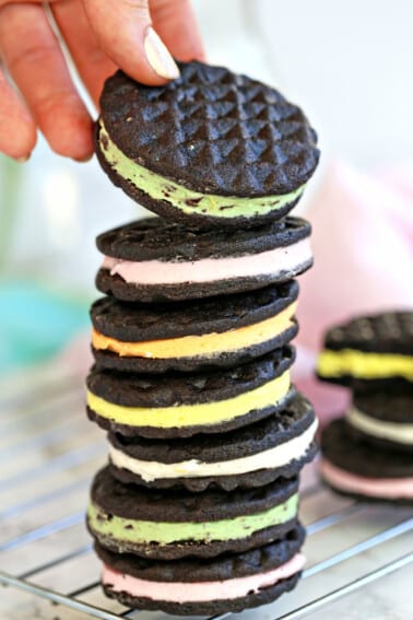 Stack of homemade Oreos with different flavors of filling with a hand pulling one off the top