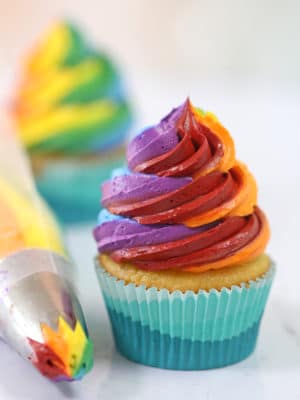 Cupcake frosted with colorful rainbow icing, with a piping bag sitting next to it.