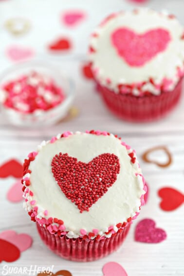 White cupcake with heart sprinkles around the edge and a heart-shaped sprinkle shape in the center