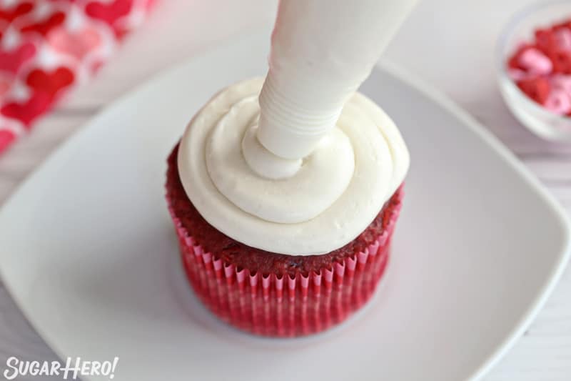 Red velvet cupcake being frosted with white buttercream