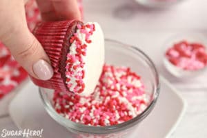 Hand dipping the edges of a frosted cupcake in heart-shaped sprinkles