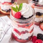 Three jars of mixed berry shortcake with berries, whipped cream, and shortcakes.