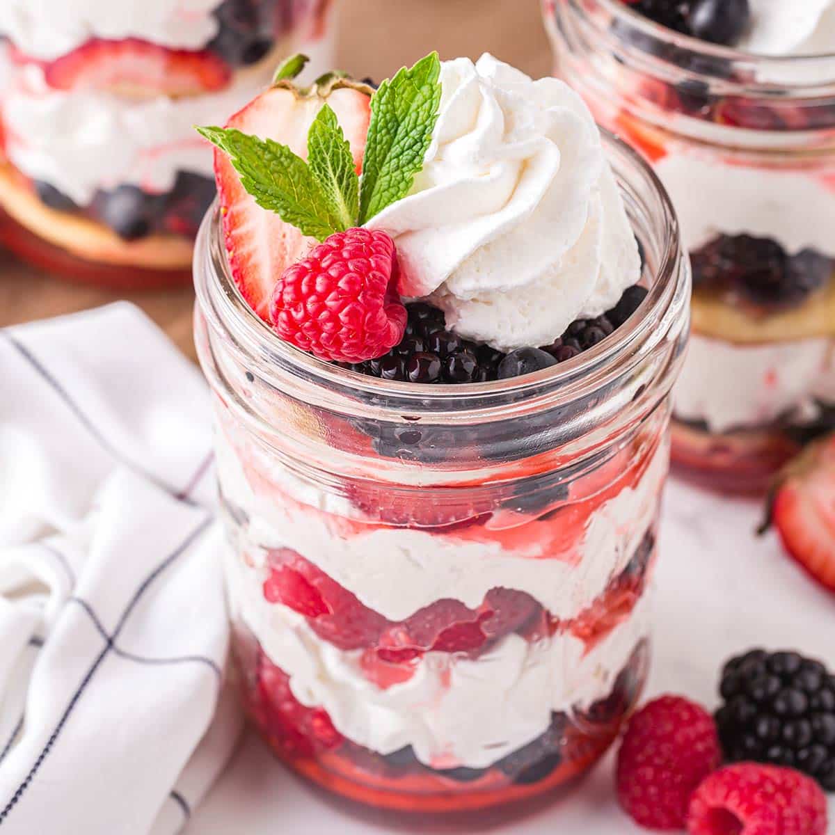 Three jars of mixed berry shortcake with berries, whipped cream, and shortcakes