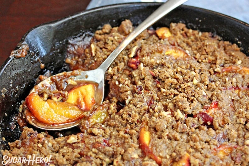 Spoon resting in skillet with scoop of peach crisp in spoon