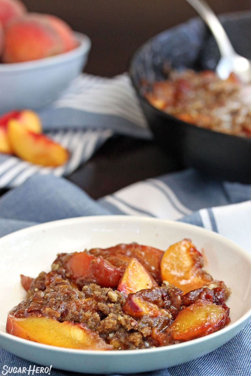 Bowl of peach crisp with cast iron skillet in background