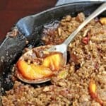 Spoon with a scoop of peach crisp from a cast iron skillet.