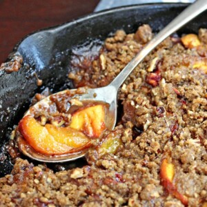 Spoon with a scoop of peach crisp from a cast iron skillet