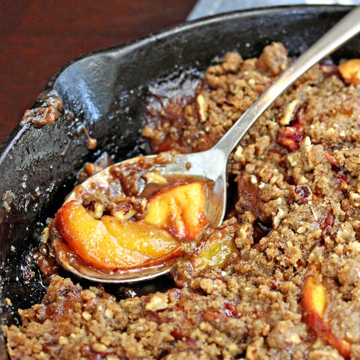 Spoon with a scoop of peach crisp from a cast iron skillet.