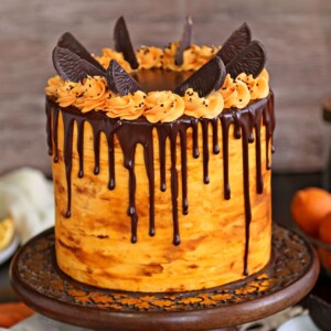 Cake with orange buttercream and chocolate ganache drip on a wooden cake stand