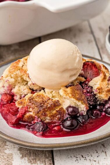 Serving of berry cobbler on a plate with vanilla ice cream on top.