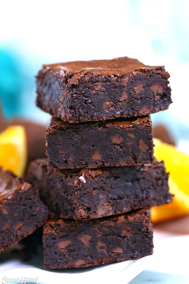 Stack of four chocolate orange brownies with orange slices in the background.