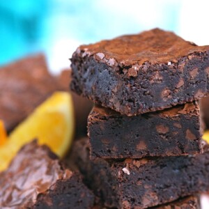 Stack of four chocolate orange brownies with orange slices alongside them.