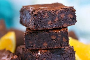 Stack of four chocolate orange brownies with orange slices in the background.