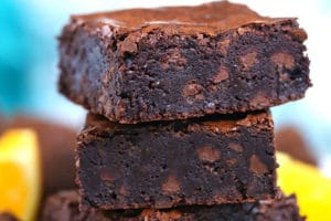 Stack of four chocolate orange brownies with orange slices in the background.