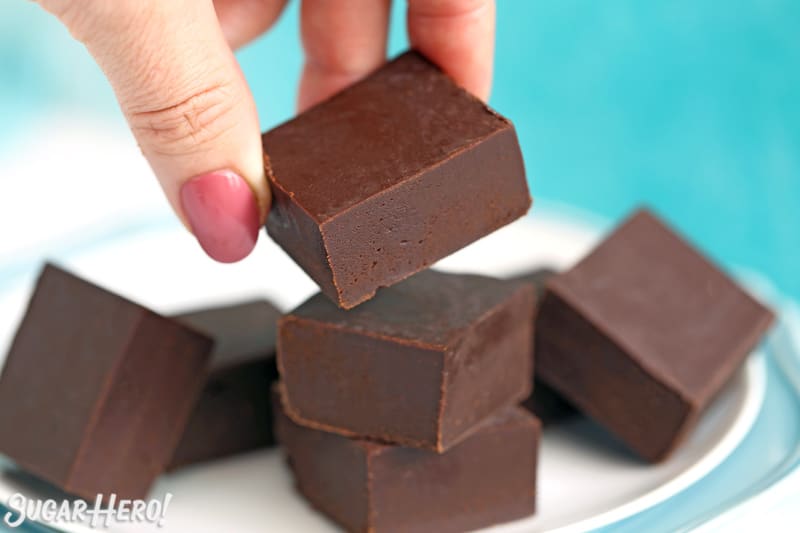 Hand picking up a piece of chocolate fudge from a white plate.